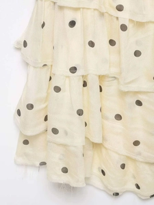 Détail de l'ourlet à volants étagés blanc crème avec pois gris foncé sur tissu en mousseline