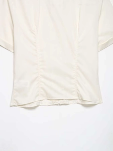 Detail of cream poplin shirt showing pleated waist seams and crisp cotton fabric texture