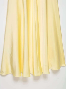 Détail d'une robe en satin jaune clair montrant la texture soyeuse et l'ourlet drapé
