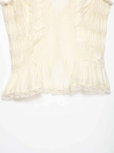 Detailed macro view of the ruffled lace hem and pleated texture on this off-white blouse
