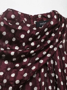 Détail d'un haut en mousseline bordeaux à pois avec texture plissée et bouton au col