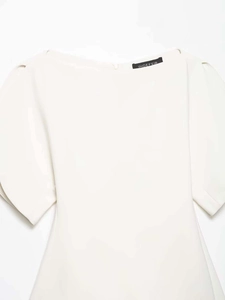 Detail of white off-the-shoulder blouse with puff sleeves and brand label on woven fabric