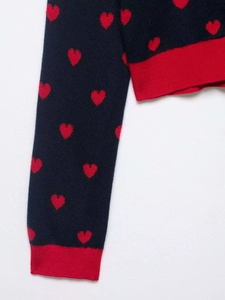 Detail of navy knit sweater featuring red heart jacquard patterns and ribbed cuffs