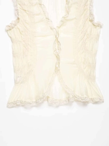 Detail of cream V-neck sleeveless top featuring delicate lace trim and white buttons