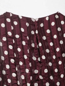 Gros plan sur un tissu mousseline plissé bordeaux à pois blancs et étiquette