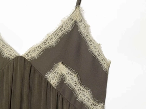 Detail of V-neckline with olive green pleated fabric and white eyelash lace trim