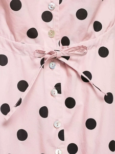 Detailed view of pink polka dot fabric with iridescent buttons and a tied waist bow
