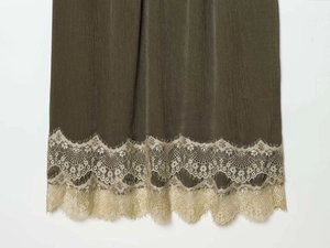 Detail of olive green pleated dress hem with elegant wide gold floral lace trim