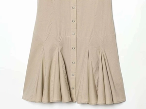 Detail of single-breasted beige dress featuring pleated hem and crisp cotton fabric texture