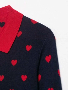 Detail view of the red contrast polo collar and heart jacquard knit pattern on the navy sweater