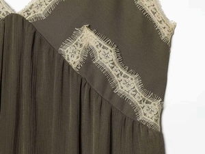 Detail of olive green pleated dress featuring white eyelash lace trim on V-neckline
