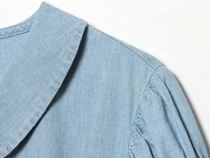 Close-up of pleated shoulder and round neck detail on light blue denim blouse