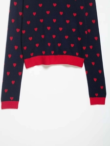 Detail of navy knit sweater with red heart jacquard and ribbed cuffs showing premium texture