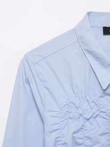 Detail view of light blue shirt showing elegant ruched texture and refined fabric quality