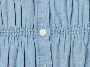 Detailed view of light blue shirt featuring a white button and smocked fabric texture