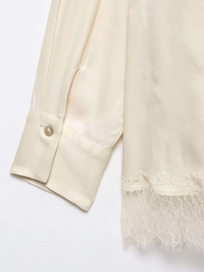 Detailed view of cream satin blouse featuring eyelash lace trim and shiny button cuffs