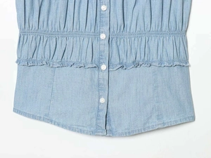 Detail of light blue denim shirt featuring elastic smocked waist and white round buttons