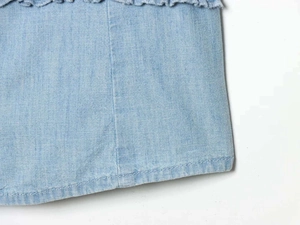 Detailed close-up of light blue denim fabric featuring ruffle edges and visible stitching