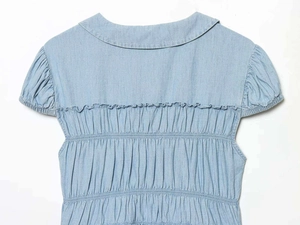 Detail of light blue denim shirt back featuring elastic shirred texture and ruffle trim