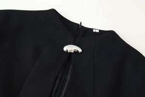 Détail de l'encolure d'une robe noire avec ornement en métal argenté et fermeture éclair