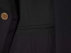 Detalle de blazer de sarga negra con un botón marrón de cuatro agujeros y bolsillo de solapa