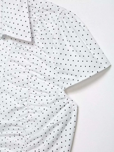 Detailed view of white polka dot short sleeve shirt with ruffled collar and pleated front