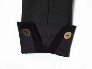 Detalle del puño de blazer negro con borde acanalado y botones decorativos marrón claro