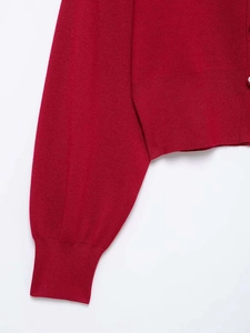 Detail of red knitted cardigan featuring ribbed cuffs and a silver metal heart button