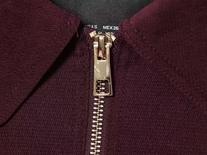 Macro shot of burgundy jacket with golden zipper detail and knit fabric texture