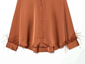 Close-up of rust red satin shirt featuring elegant feather cuffs and buttons