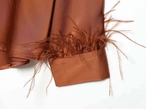 Close-up of brown satin shirt cuff featuring elegant feather trim and silk-like shine