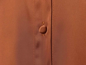 Detail of a rust-colored satin blouse showing a matching fabric-covered button and stitching