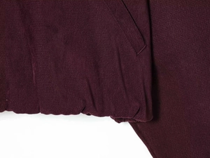 Detailed close-up of burgundy knit fabric texture with elastic hem and side pocket seam