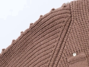 Detail of brown ribbed knit cardigan featuring wavy edges and sparkling rhinestone buttons