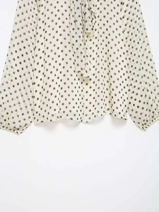 Detailed view of the sheer dotted chiffon fabric with elegant neck tie on a beige blouse