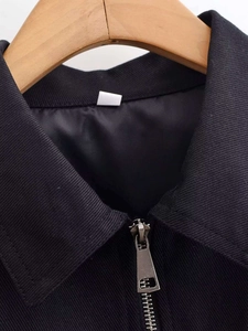 Macro detail of a black textured jacket featuring a metallic silver zipper and wooden hanger