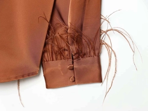 Detail of satin shirt cuff in brown with ostrich feather trim and two matching buttons