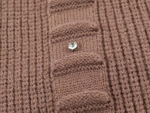 Detailed close-up of brown knit cardigan featuring vertical ribbing and a rhinestone button