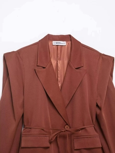 Detail of rust brown oversized blazer with shoulder pads and waist belt cinching the silhouette