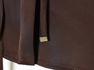 Detail of satin shirt showing golden metal aglets on waist ties with fine stitching