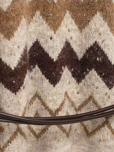 Macro detail of V-neck knitwear featuring multi-color chevron patterns and a leather belt