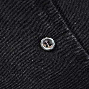 Close-up of a dark grey four-hole button on black washed denim fabric with twill texture