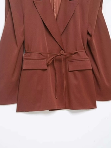 Detail of waist-cinching tie and flap pockets on rust red tailored blazer jacket