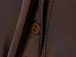 Macro shot of dark brown satin shirt button and high-quality twill fabric texture