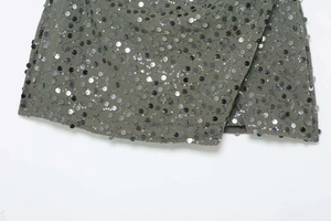 Détail d'une mini-jupe gris-vert avec paillettes argentées ondulées et ourlet croisé