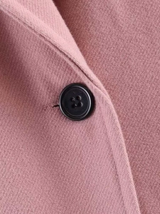 Detail of pink wool blend coat fabric with a classic black four-hole sewing button