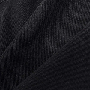 Detailed close-up of premium black twill denim fabric texture on the asymmetrical jacket