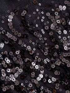 Detail shot of black sequins sewn onto twill fabric with wave-like decorative patterns