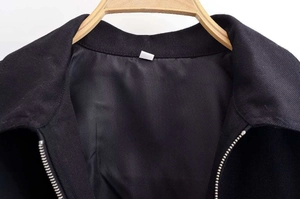 Detail of a black sequin-trimmed jacket collar with silver zipper on a wooden hanger
