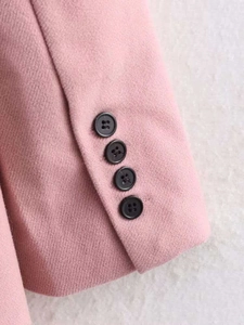Detailed view of pink wool coat sleeve featuring four black buttons and premium twill texture